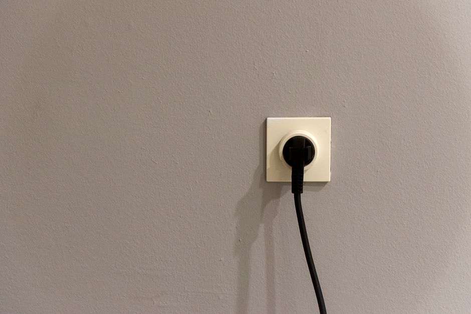 Asmuo apžiūri rozetę ir laidus, prie jos aiški elektros saugos kontrolė